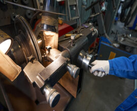 Man in blue protective clothes and gloves standing near table and working on the machine with car parts