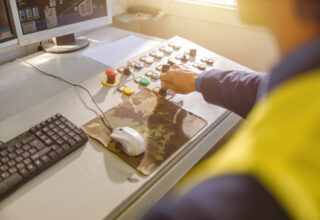 Close up of man factory worker sitting at the table with desktop computer and turning key on control panel